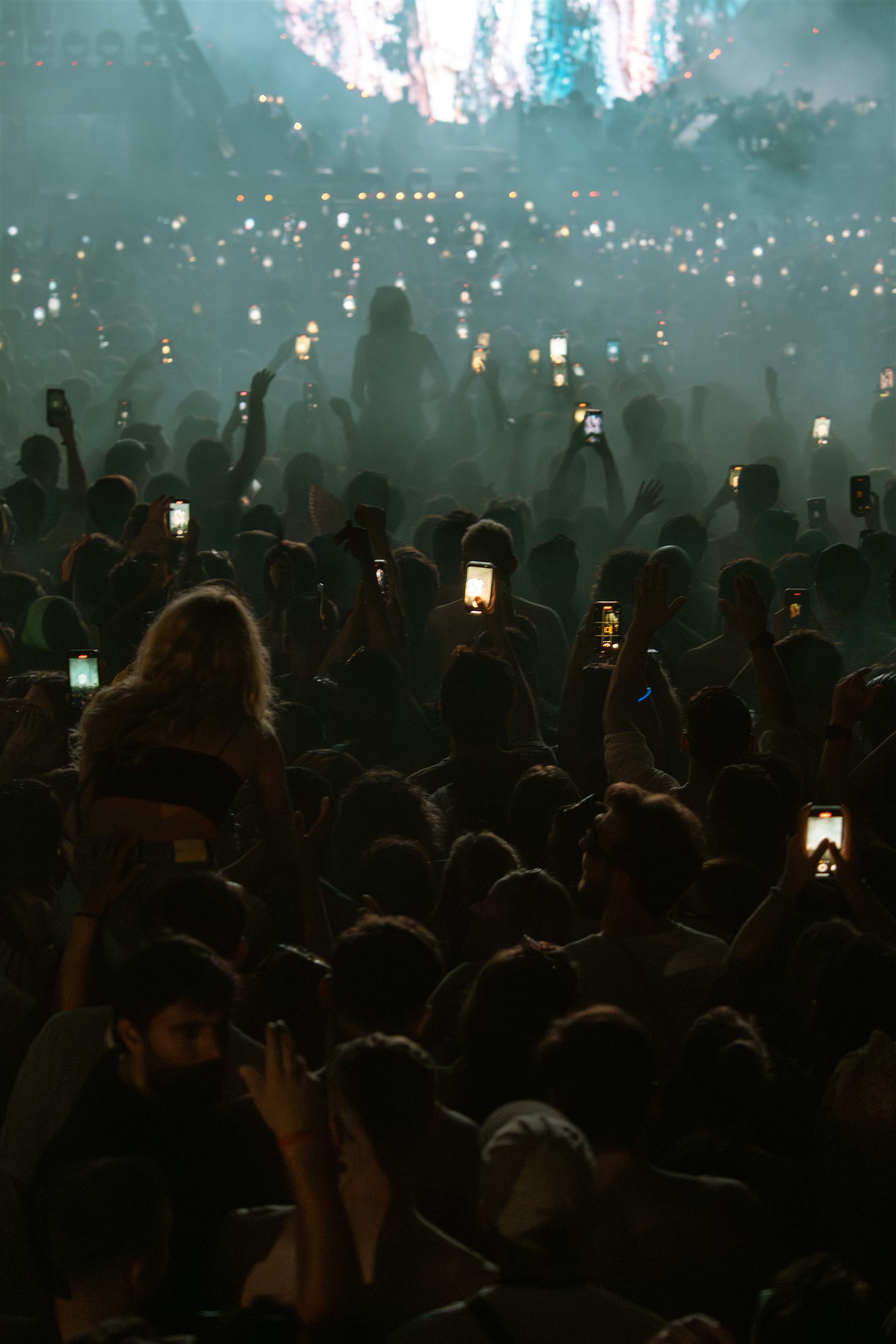 Público con los móviles en alto entre el humo del escenario, de noche